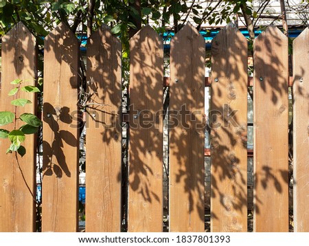 Fence palisade fence on blue sky background. Pointed logs, old wood texture.Shadows from tree branches and leaves on the fence