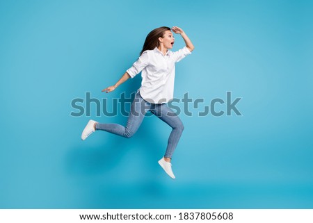 Full length photo lady jump high running look far away interested wear white shirt jeans shoes isolated blue color background