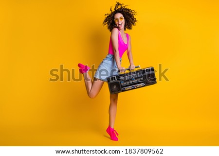 Full size photo of attractive lady hold retro boom box recorder chill students event holiday rejoice enjoy music wear sun specs pink singlet denim skirt shoes isolated yellow color background