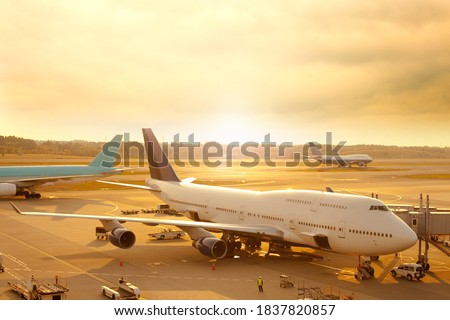 Airplane being prepared for departure at the tarmac of an airport at sunrise.