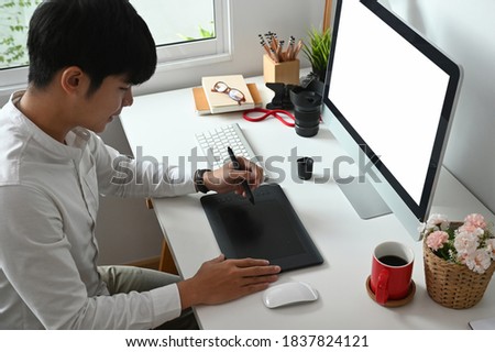Young Asian graphic designer working on computer and graphics tablet in his working space.