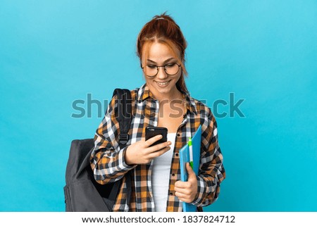 Teenager student Russian girl isolated on blue background sending a message with the mobile