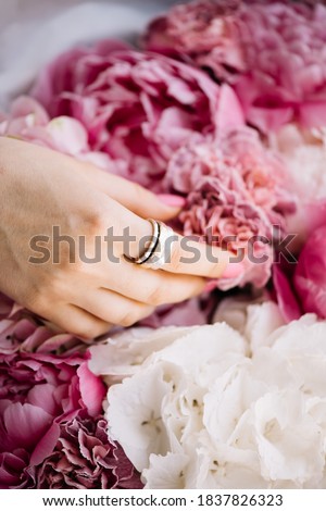 Woman's hand touching beautiful pink and white peony flowers, showing her ring on a finger 