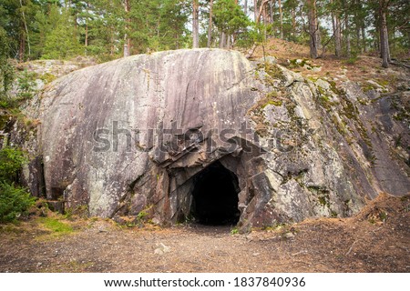 Landscape with cave and forest. Scenic entrance to cave. Rock wall with a dark hole. Spro, Mineral historic mine. Nesodden Norway. Nesoddtangen peninsula. Royalty-Free Stock Photo #1837840936