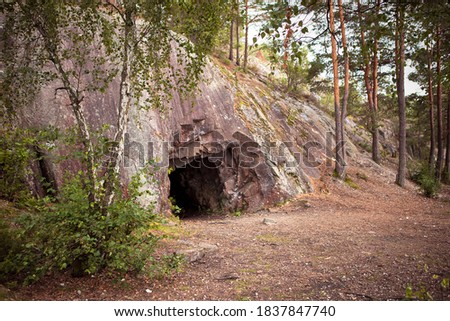 Landscape with cave and forest. Scenic entrance to cave. Rock wall with a dark hole. Spro, Mineral historic mine. Nesodden Norway. Nesoddtangen peninsula. Royalty-Free Stock Photo #1837847740