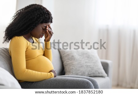 Young pregnant black woman suffering from headache or migraine, feeling sick, sitting on sofa at home, free space. Sad african american expecting lady touching her forehead and big tummy, home alone Royalty-Free Stock Photo #1837852180
