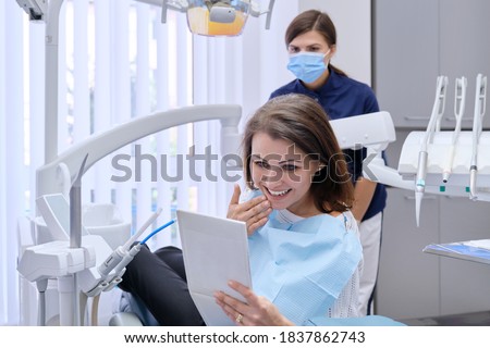 Happy middle aged woman with doctor dentist looking in mirror at teeth, sitting in dental chair. Medicine, dentistry and health care concept Royalty-Free Stock Photo #1837862743
