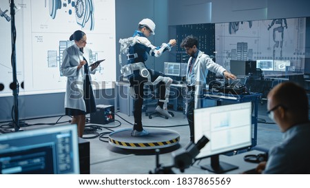 In Robotics Development Laboratory: Engineers and Scientists Work on a Bionics Exoskeleton Prototype with Person Testing it. Designing Wearable Exosuit to Help Disabled People, Warehouse Workers Royalty-Free Stock Photo #1837865569