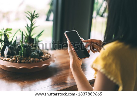 Close up of adult female hand using mobile phone for digital application online on day. Blank screen device for message. Backgroud at cafe with blur cactus.