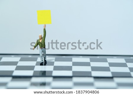 Miniature people toys photography - demonstrator standing with blank text banner sign above chessboard 