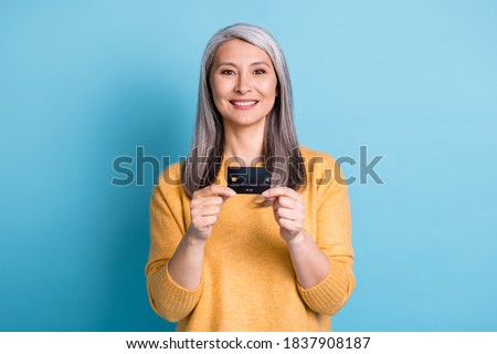 Photo of positive old woman hold credit card enjoy easy bank saving money profit wear style trendy pullover isolated over blue color background