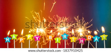 Burning candles with the words Happy Birthday, burning in a long row. Bengal fire sparkle, sparkler candle on multicolored background. Happy Birthday card design concept. panoramic image