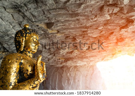 Image of Lord Buddha with gold leaves and Gilding to cover to face and body of Buddha statue in the cave that Buddhist show to worship with reflect lighting background at Wat Khao Tamtiem,Thailand.