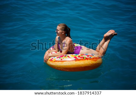 Beautiful happy young woman in a swimsuit with an inflatable ring relaxing in the blue sea. Sunny day, seaside vacation, tourism