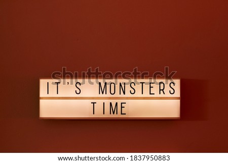 It's Monsters Time text displayed on a LED lightbox red ambient light in the room, medium close-up