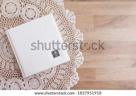 White photo book with leather cover. Stylish wedding photo album.  Family photoalbum on the table . Beautiful notepad or photobook with elegant openwork embossing on a wooden background.