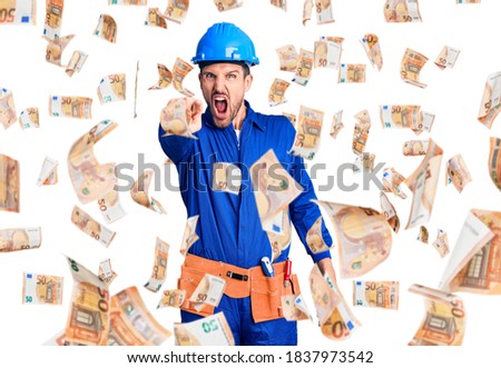 Young handsome man wearing worker uniform and hardhat angry and mad screaming frustrated and furious, shouting with anger. rage and aggressive concept.