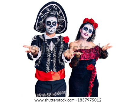 Young couple wearing mexican day of the dead costume over background smiling cheerful with open arms as friendly welcome, positive and confident greetings 