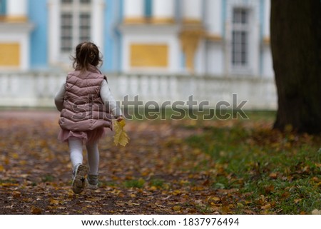 Blurred photo of a long-haired little girl running along an autumn road in a park. A cheerful girl in a pink vest, skirt and white tights.