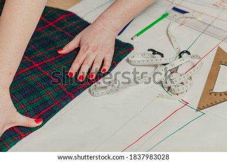 Designer creates a model. Female hands with a manicure make markings on a piece of Scottish fabric
