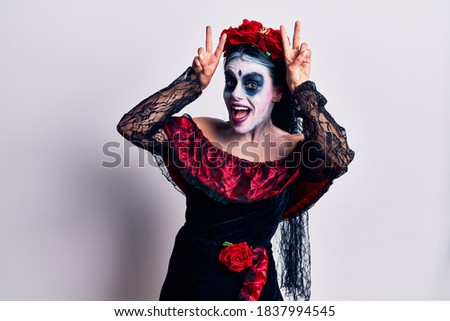 Young woman wearing mexican day of the dead makeup posing funny and crazy with fingers on head as bunny ears, smiling cheerful 