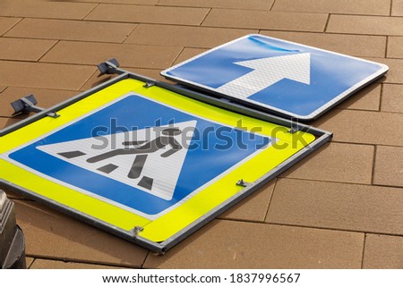 Damaged fallen pedestrian crossing road signs and direction arrow on city street