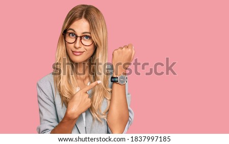 Beautiful blonde young woman wearing business clothes in hurry pointing to watch time, impatience, looking at the camera with relaxed expression  Royalty-Free Stock Photo #1837997185