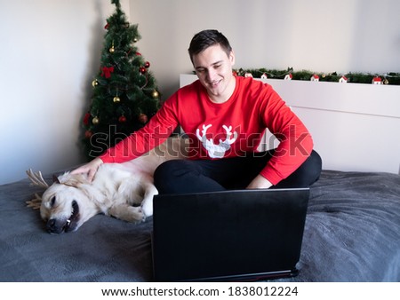 A man in a medical mask with a dog looks at the laptop screen. Christmas video greetings on social networks. New Year's home holiday. Coronavirus (COVID-19.