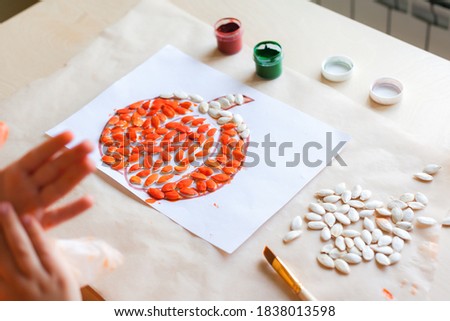 Making pumpkin from seeds on white paper, Halloween DIY concept. Step by step instruction. Step 3 Paint pumpkin seeds with orange color