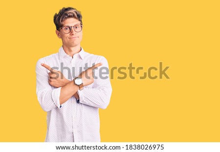 Young handsome man wearing business clothes and glasses pointing to both sides with fingers, different direction disagree 
