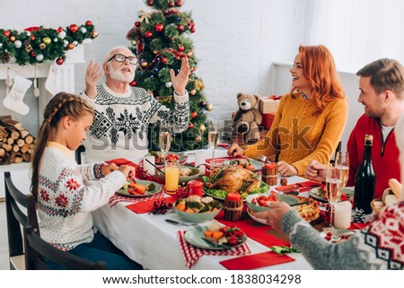 Family sitting at festive table with thanksgiving dinner near fireplace at home