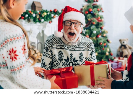 excited senior man in santa hat taking christmas presents from grandchildren Royalty-Free Stock Photo #1838034421