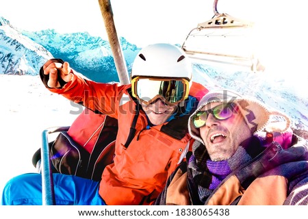 Best friends having fun taking selfie at chairlift with snowboard equipment on mountain ski resort - Winter friendship concept with young people ready to ride down the slope - Bright vivid filter Royalty-Free Stock Photo #1838065438