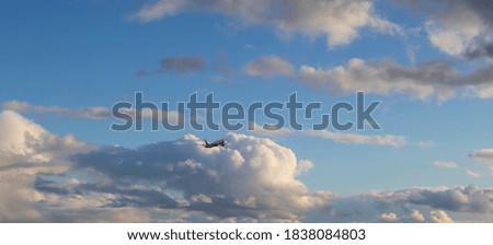 An airplane flies in the blue sky between the clouds