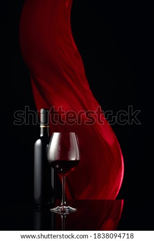 Вottle and glass of red wine on a black reflective background. Red cloth flutters in the background. Copy space.
