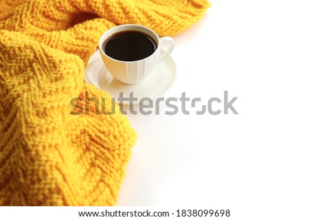 White porcelain cup with black coffee on the knitted yellow scarf and white background. Sweet home winter concept. Simple template for your postcard and design, place for text