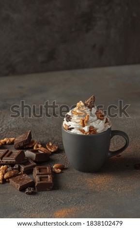 Hot chocolate in mug decorated with whipped cream, chocolate slices and nuts on concrete background. Traditional beverage for cold days concept.