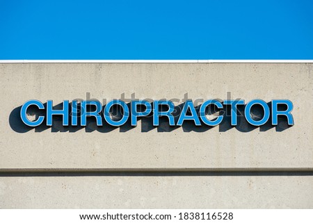 Chiropractor sign in blue letters on commercial building exterior. Blue sky.