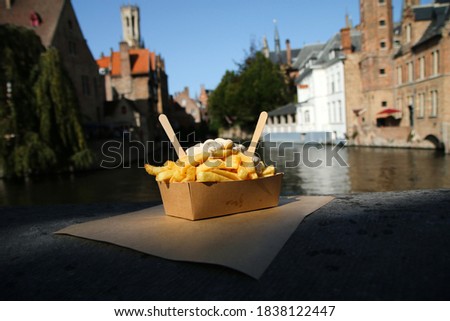The traditional street food snack, the Belgian Fries with pepper sauce pictured on the wall over the channel in Bruges in Belgium. 