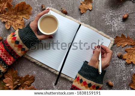 Autumn composition made of brown dried leaves and acorns on dark concrete background. Template mockup blank notebook and hand with a pen and cup of coffee. Fall, halloween. Flat lay, copy space
