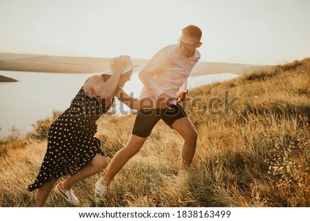 young man and woman walking in the meadow at sunset in summer near the lake. A couple of fair-haired fair-skinned people in love are resting in nature in a field at sunset.