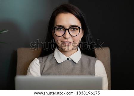 remote work remotely in the office coworking on a laptop computer gadget, smart brunette woman looks at the camera in a white shirt. Manager in the banking sector, glasses on the face
