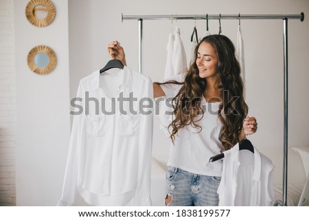 Beautiful young woman stylist standing near rack with hangers with white clothes. Shopaholic with many clothes on white background.
 Royalty-Free Stock Photo #1838199577