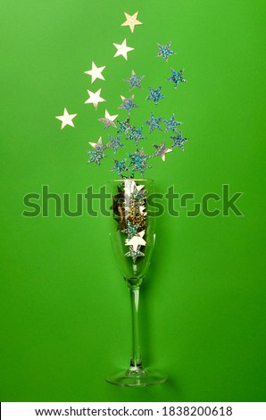 Vertical image.One champagne glass and shiny confetti on the bright surface
