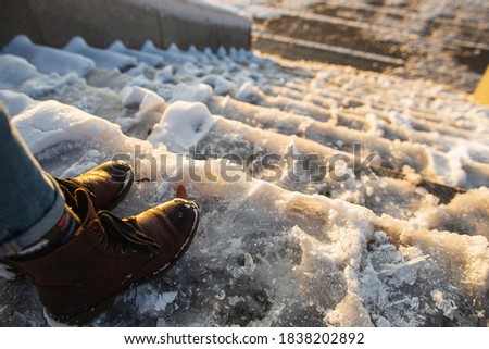 Danger of slipping. Female boots on rough slipper ice surface. A woman in brown leather shoes descends the slippery ice ladder. Royalty-Free Stock Photo #1838202892
