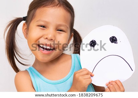 Happy vs sad. Little girl smiling holding a frown face picture.