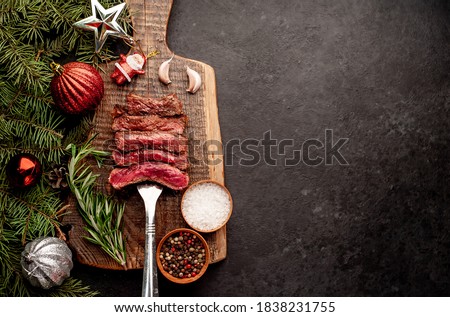 
Different degrees of roasting of steak on a meat fork for Christmas on a background of a stone with a spruce and Christmas toys with copy space for your text