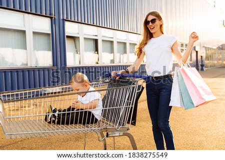 Excited young mother with a child and shopping bags fun running with a shopping trolley on the street near a shopping center