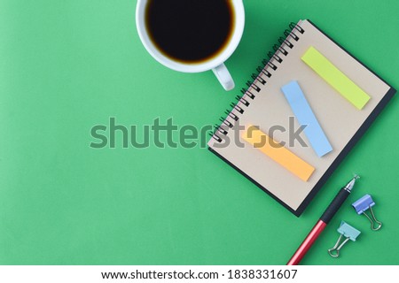 Flatlay view of school and office stationary isolated on a green background. Notebook, pen, paper clips and hot coffee. Education, business and workplace concept. Copy space for text