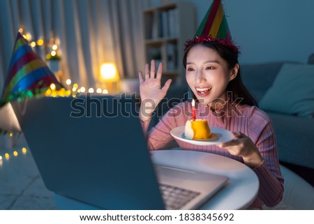 asian young woman wearing birthday hat has video chat online by laptop while celebrating and giving cake for her friend